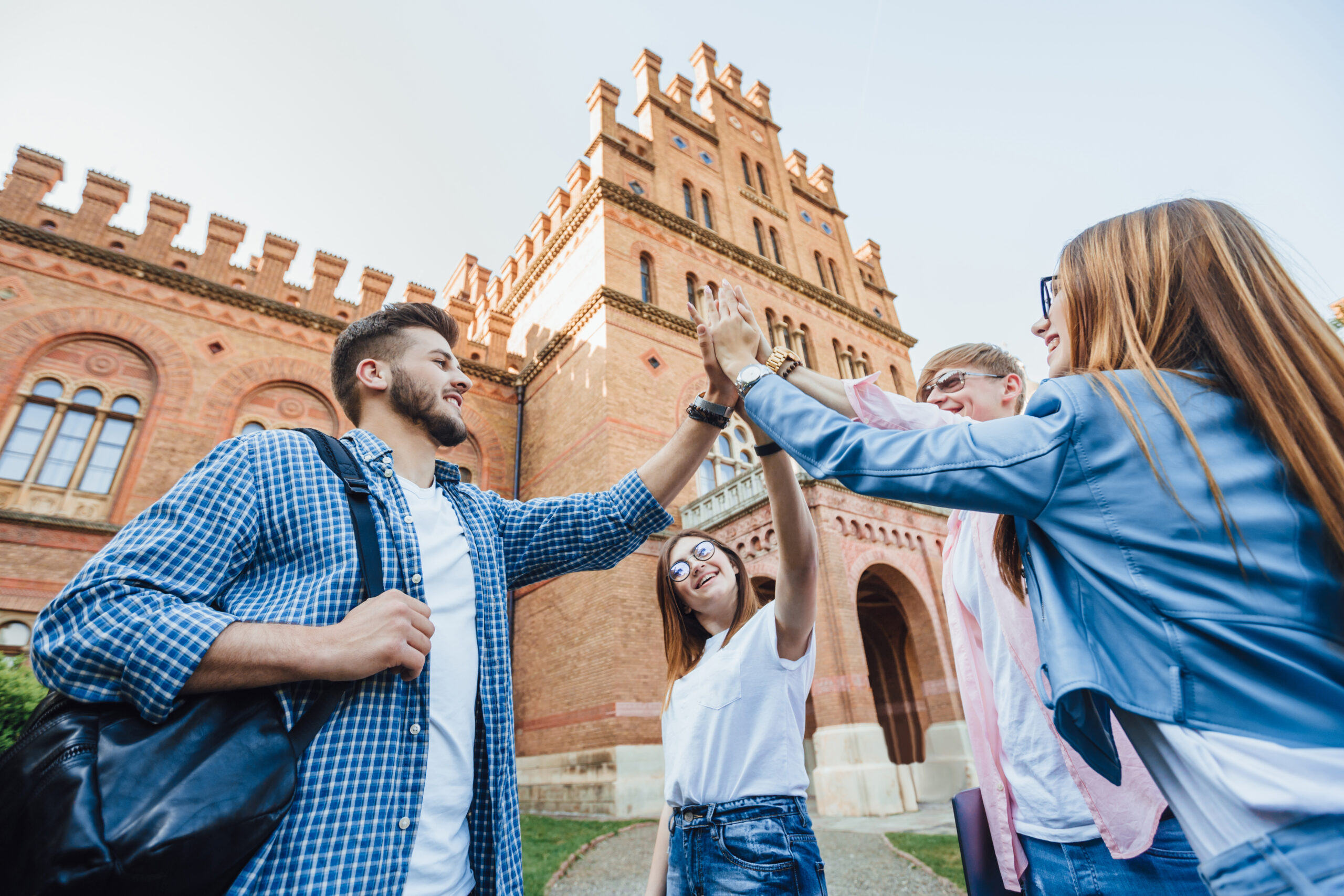 Low angle of cheerful team of students passed the test by preparing all together. Success, fun, friendship, education concept. Four graduates are celebrating outside. Casual clothes.
